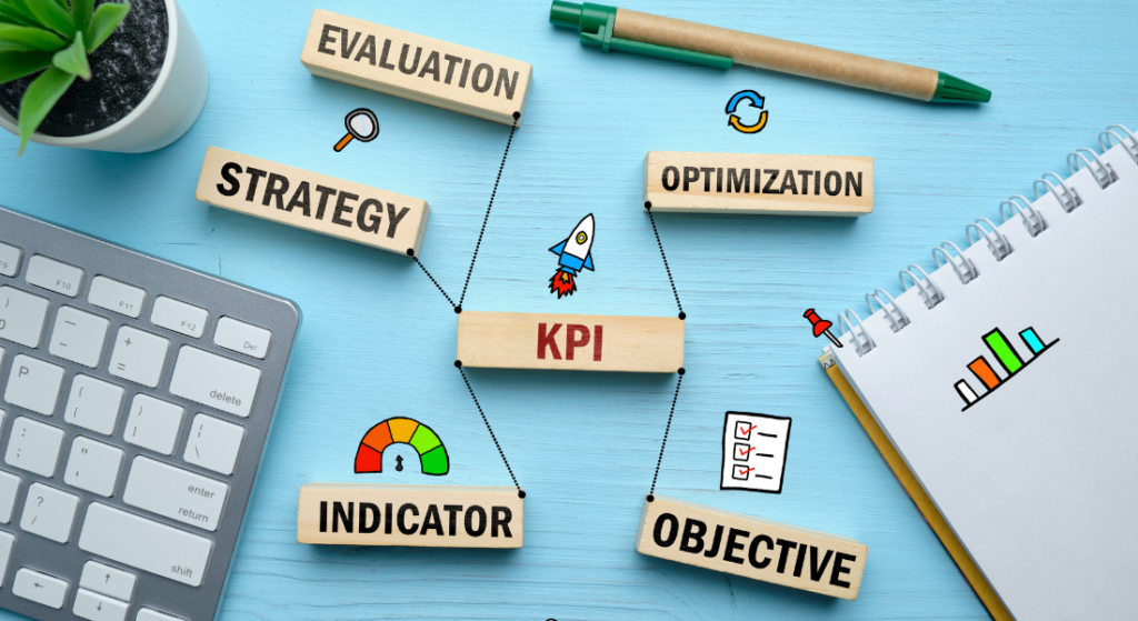 Key performance Indicator - KPIs A flat lay of a workspace featuring blocks labeled KPI, Strategy, Evaluation, Optimization, Indicator, and Objective, with a notepad and plant.